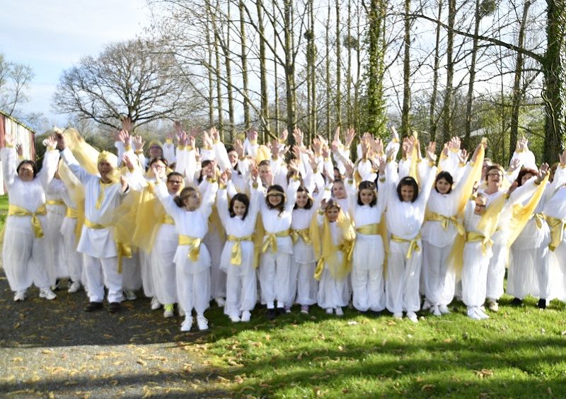 Un grand groupe en costumes blancs et jaunes, bras levés, dans un parc.
