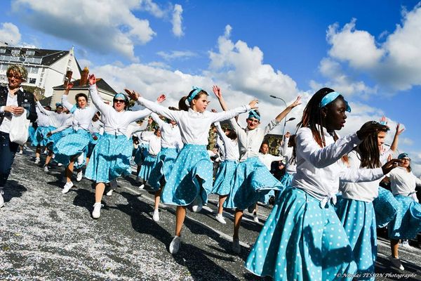 Des danseuses en jupes turquoise à pois défilent dans la rue.