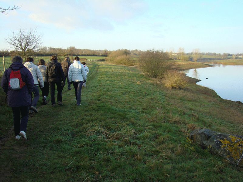 Les randonneurs longent un lac, sur une digue herbeuse.